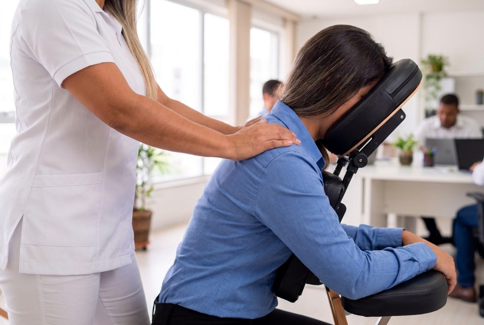 Massoterapeuta de jaleco branco atendendo colaborador sentado e vestido durante quick massage em ambiente de escritório